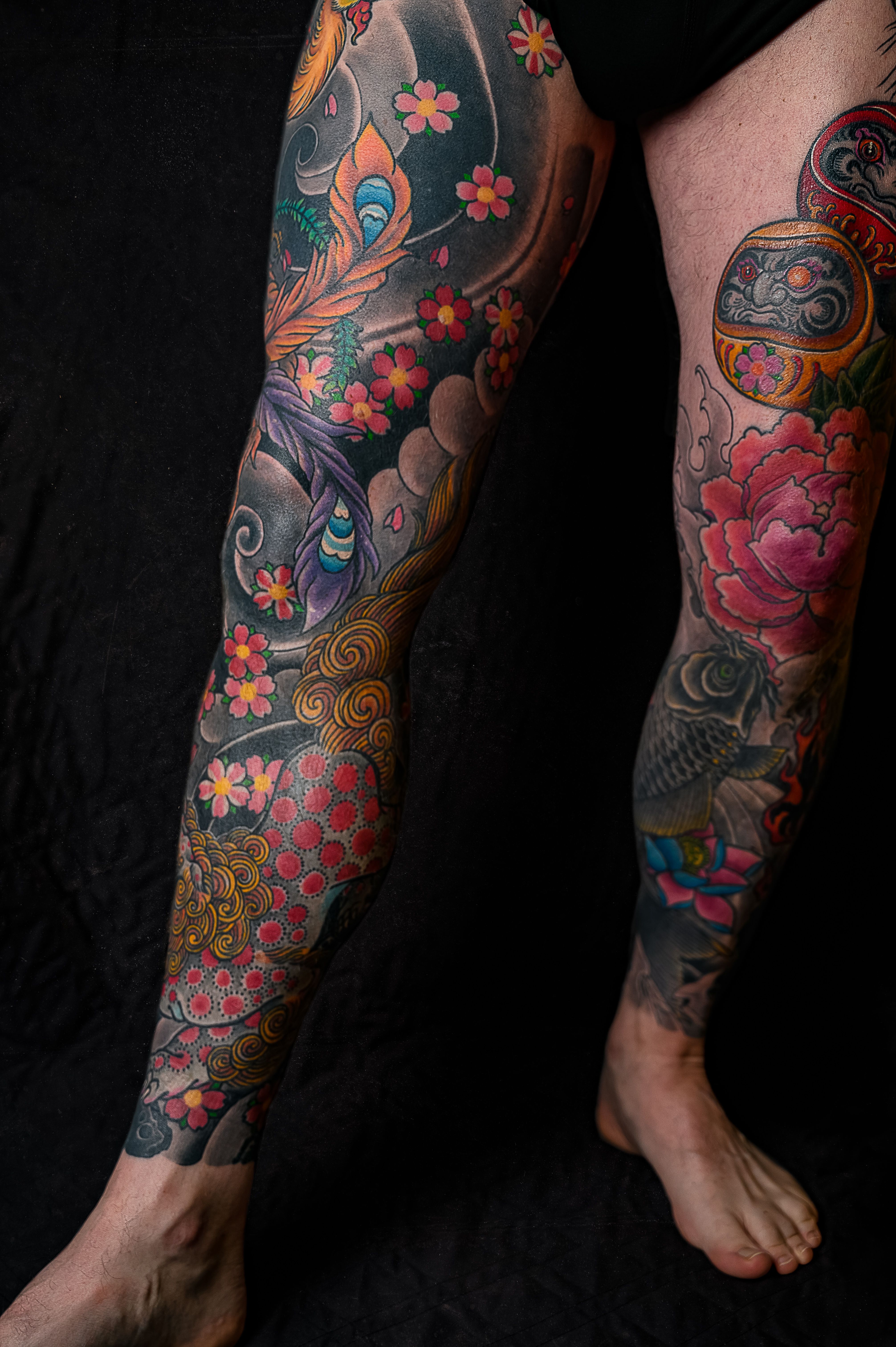 Pernas com irezumi completo mostrando composição japonesa com sakura, fênix e carpa